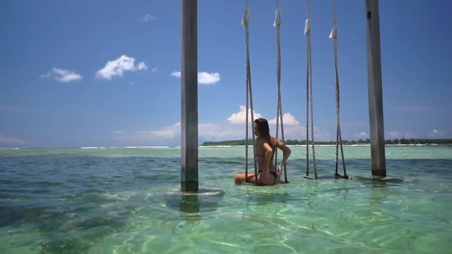 Ocean shot with beautiful woman on the swing located in the crystal ocean water