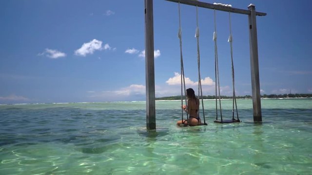 Brunette woman seats on the swing in beautiful crystal water in the ocean water, vacation concept