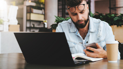 Obraz premium Businessman sitting in cafe, using smartphone, working on laptop, freelancer working in coffee shop.Education for adult.