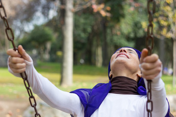 Radiant mature woman having fun swinging in the playground during autumn season. Middle aged lady dreaming as a child girl. Young spirit concept