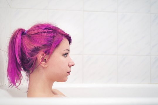 Beautiful young woman with pink hair in bathtub