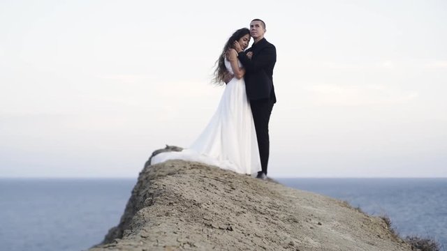 Side view of wedding couple in white dress and black suit standing on eart path at blue sky background Crimea, Chameleon cape, Koktebel