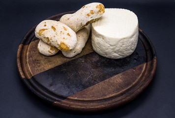 Cheese bread and brazilian minas white cheese on a wooden cutting board isolated in dark background
