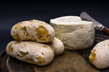 Cheese bread and brazilian minas white cheese on a wooden cutting board isolated in dark background