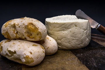 Cheese bread and brazilian minas white cheese on a wooden cutting board isolated in dark background
