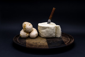 Cheese bread and brazilian minas white cheese on a wooden cutting board isolated in dark background