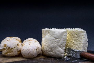 Cheese bread and brazilian minas white cheese on a wooden cutting board isolated in dark background