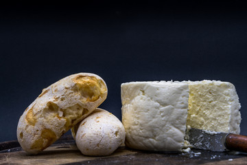 Cheese bread and brazilian minas white cheese on a wooden cutting board isolated in dark background