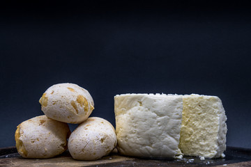 Cheese bread and brazilian minas white cheese on a wooden cutting board isolated in dark background