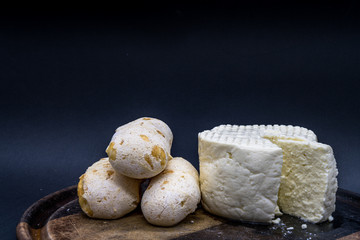 Cheese bread and brazilian minas white cheese on a wooden cutting board isolated in dark background