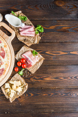 Food background design. Big pizza with ham and mushrooms on a round cutting board on a dark wooden background. Pizza Ingredients.