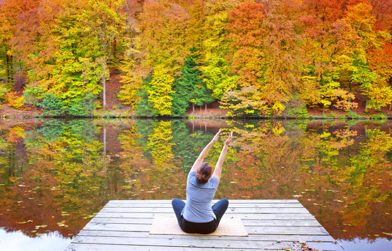 Woman meditating outdoors in the autumn park near forest lake.