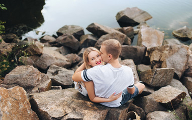 Young boy and girl are hugging on the background of stones and small river. Beautiful love story of newlywed lovers.