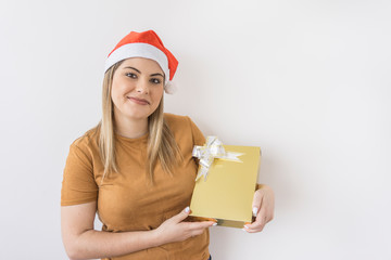 Young woman smiling wearing Christmas hat, holding a golden gift box on white background