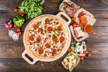 Large meat pizza with bacon, sausage, salami, pepperoni and olives and on a round cutting board on a dark wooden background. Pizza ingredients