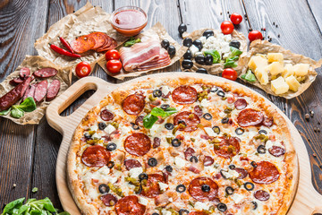 Large meat pizza with bacon, sausage, salami, pepperoni and olives and on a round cutting board on a dark wooden background. Pizza ingredients