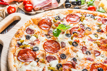 Large meat pizza with bacon, sausage, salami, pepperoni and olives and on a round cutting board on a dark wooden background. Pizza ingredients