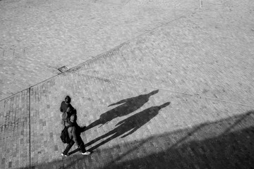 Blurred unrecognizable couple from above walking on an open space square with shadows projecting on...