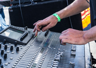 Hands in action on a mixing board adjusting the sound by pushing buttons & turning the knobs