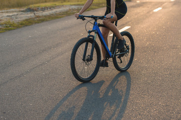 Fototapeta na wymiar A girl riding a mountain bike on an asphalt road, beautiful portrait of a cyclist at sunset 