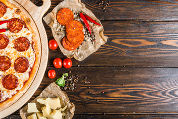 Food background design. Pizza with salami and pepperoni sausage on a round cutting board on a dark wooden background. Pizza Ingredients. Top view