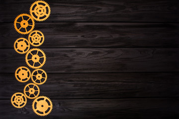 Border of gold gears on a black wooden background. View from above