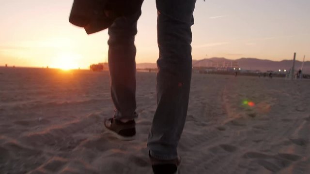 Tracking behind man on beach walking towards setting sun