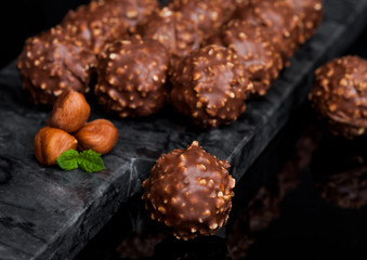 Luxury chocolate candies with hazelnuts pieces and mint leaf on black marble board.