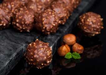 Luxury chocolate candies with hazelnuts pieces and mint leaf on black marble board.