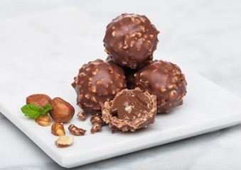 Luxury chocolate candies with hazelnuts pieces and mint leaf on marble board.