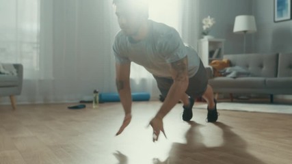 Slow Motion shot of a Strong Athletic Fit Man in T-shirt and Shorts Doing Clapping Push Up Exercises at Home in His Spacious and Bright Living Room with Modern Interior.