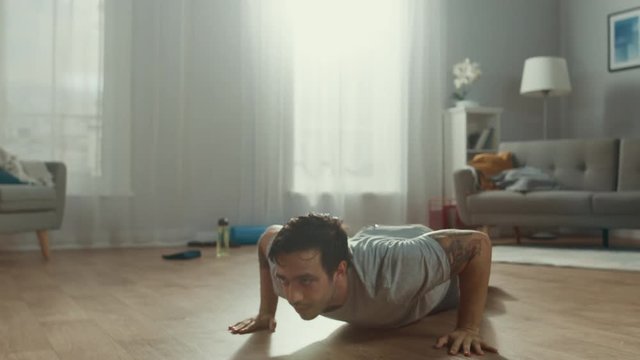 Slow Motion shot of a Strong Athletic Fit Man in T-shirt and Shorts Doing Clapping Push Up Exercises at Home in His Spacious and Bright Living Room with Minimalistic Interior.