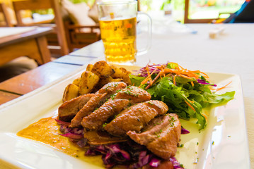 Close-up on duck breast and potatoes dish with cold beer in background
