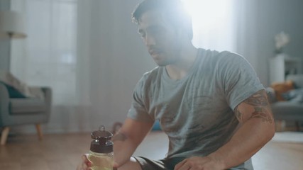 Happy and Satisfied Muscular Athletic Fit Man in T-shirt and Shorts is Drinking Water After Morning Exercises at Home in His Spacious and Bright Apartment with Minimalistic Interior.