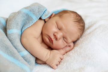 Little newborn baby boy sleeping in white blanket, lying on bed.