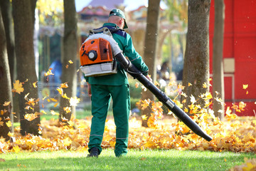worker in the Park cleans the grass from fallen leaves with the help of a wind turbine