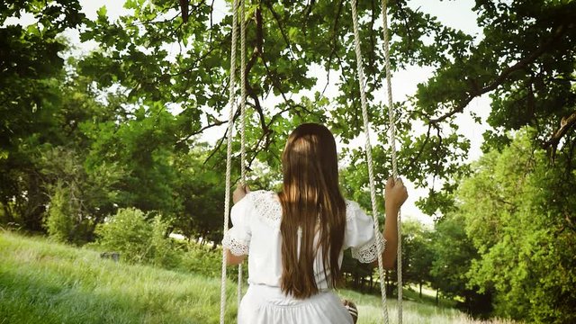 girl swinging on tree branch on swing in park. Slow motion.