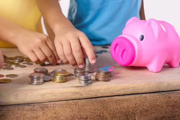 Hands of children are helping putting coins into piggy bank