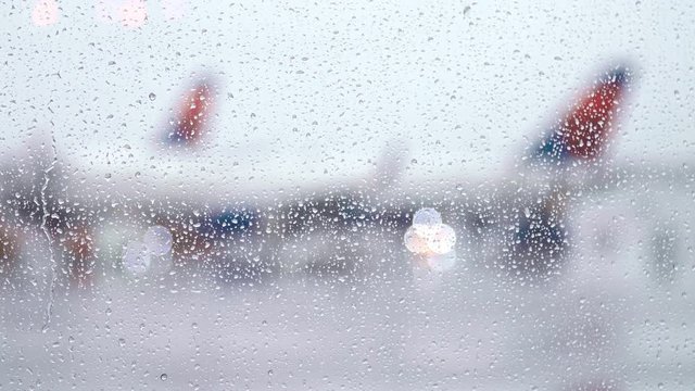Raindrops fall on bright window as airplane taxis along tarmac on rainy day