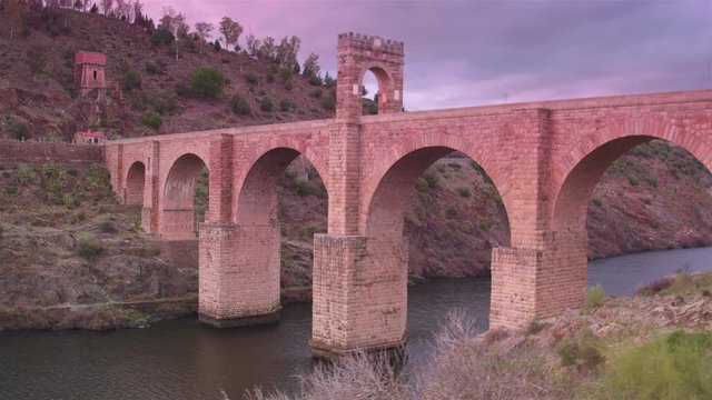 Cinematic wide tracking shot of Alc&radic;&deg;ntara Bridge at sunset