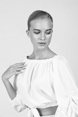 Graceful blonde with a smooth haircut poses in the studio. Light tone, high key. Highlighter in make-up. Black and white photo.

