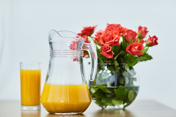 A glass of orange juice with a jug. Bouquet of roses. Flowers.