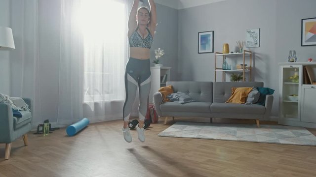 Fit Beautiful Athletic Girl in Workout Clothes is Doing Jack Burpee Exercises in Her Bright and Spacious Living Room with Minimalistic Interior.