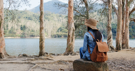 Woman sit on the tree root and enjoy the view of the lake