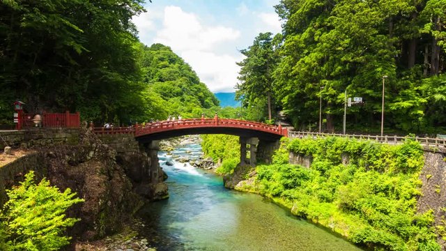 Tourists walking over the ancient Shinkyo Sacred Bridge, a Unesco World Heritage, part of Futarasan Shrine on a beautiful blue sky day in Nikko, Japan. Zoom out 4k time-lapse at 30fps