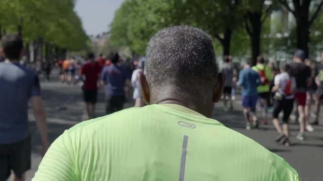 Slow motion tracking shot of a middle aged man running the marathon, shot from behind