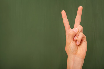 Hand in front of a green chalk board showing a victory or peace sign