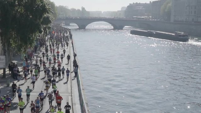 Marathon runners on river seine banks in Paris. parisian bridge and peniche boat in the background.