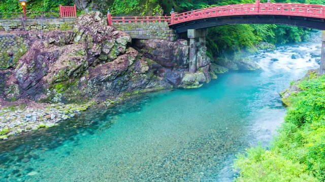 Day to night transition time-lapse of mist flowing under beautiful red Shinkyo Sacred Bridge with spotlights and flowing river, nobody present in Nikko, Japan. Panning 4k at 30fps