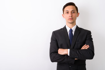 Studio shot of young handsome businessman with arms crossed agai